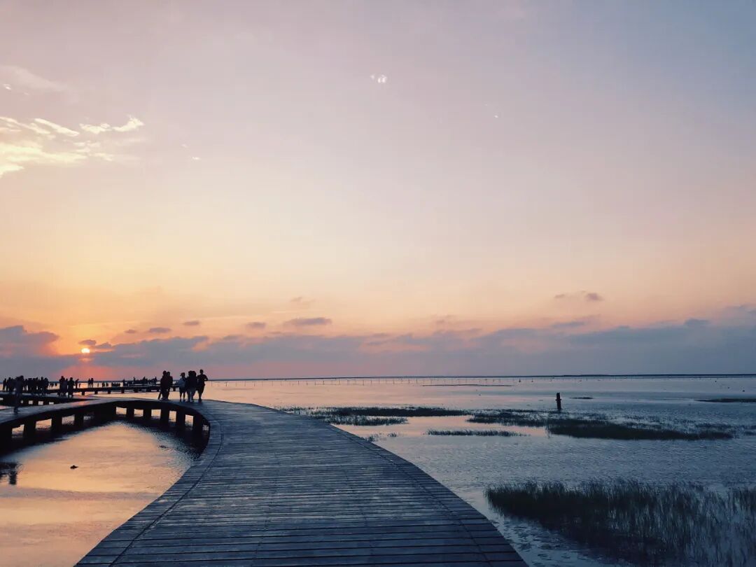 Expansive panoramic view of Gaomei Wetlands at sunset, showcasing tidal flats, boardwalk, and distant wind turbines.