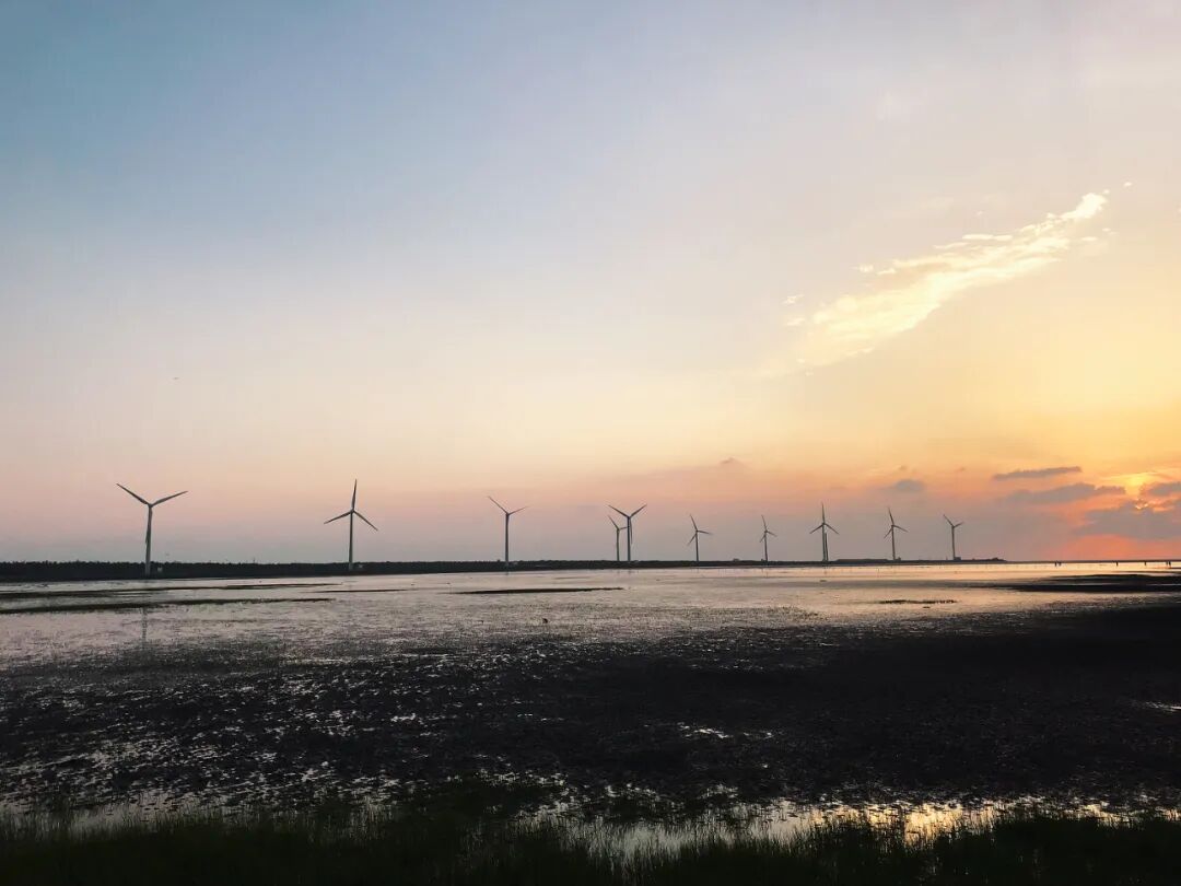 Silhouetted figures leisurely stroll the Gaomei Wetlands boardwalk, heading towards a breathtaking sunset.