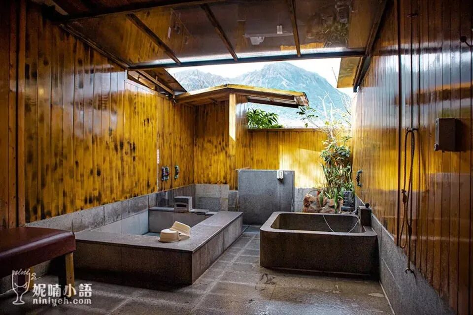 A person relaxing in a modern hot spring pool with a panoramic view of lush mountains.