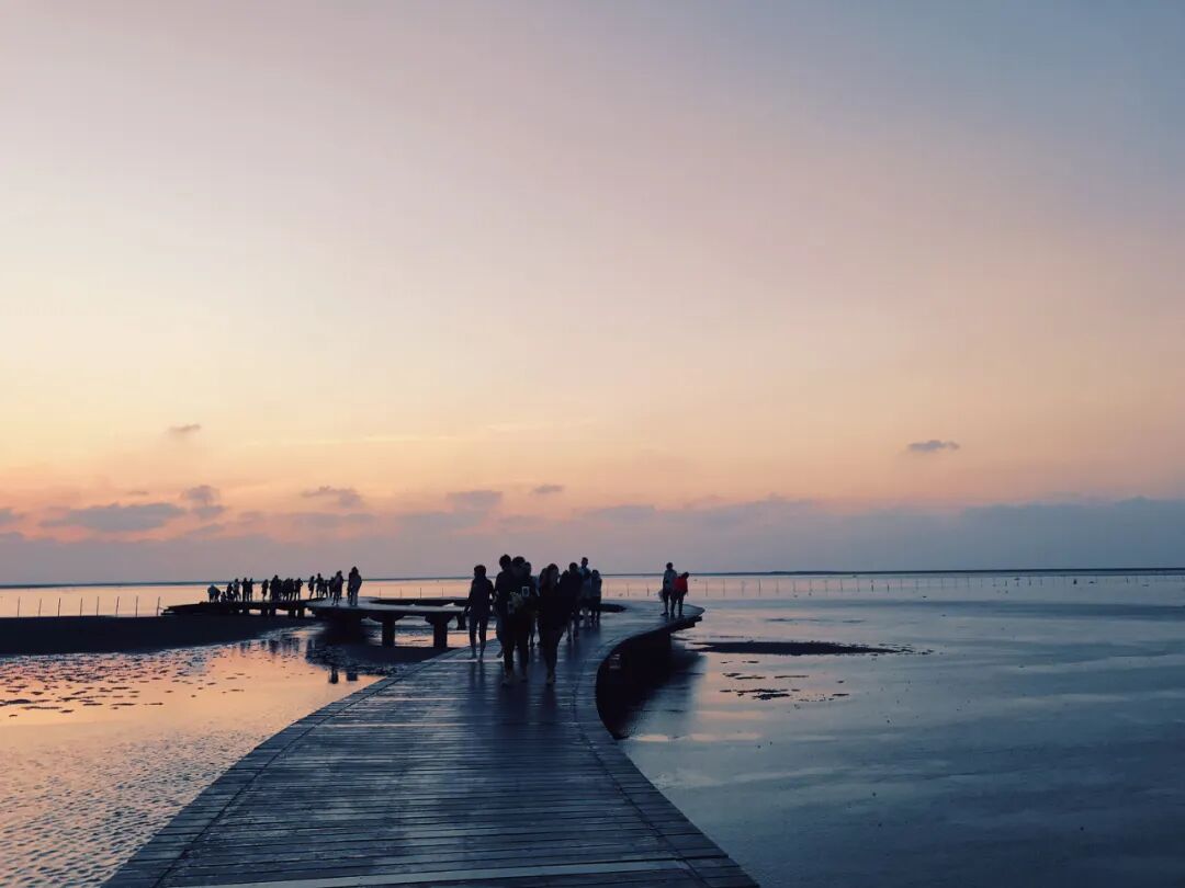 People enjoying a serene stroll along the Gaomei Wetlands boardwalk at sunset, taking in expansive views.