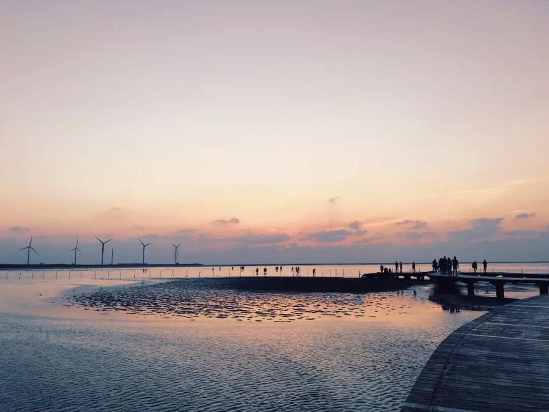 Long exposure capturing Gaomei Wetlands' tranquil beauty at sunset, with perfect mirror-like reflections on tidal flats.