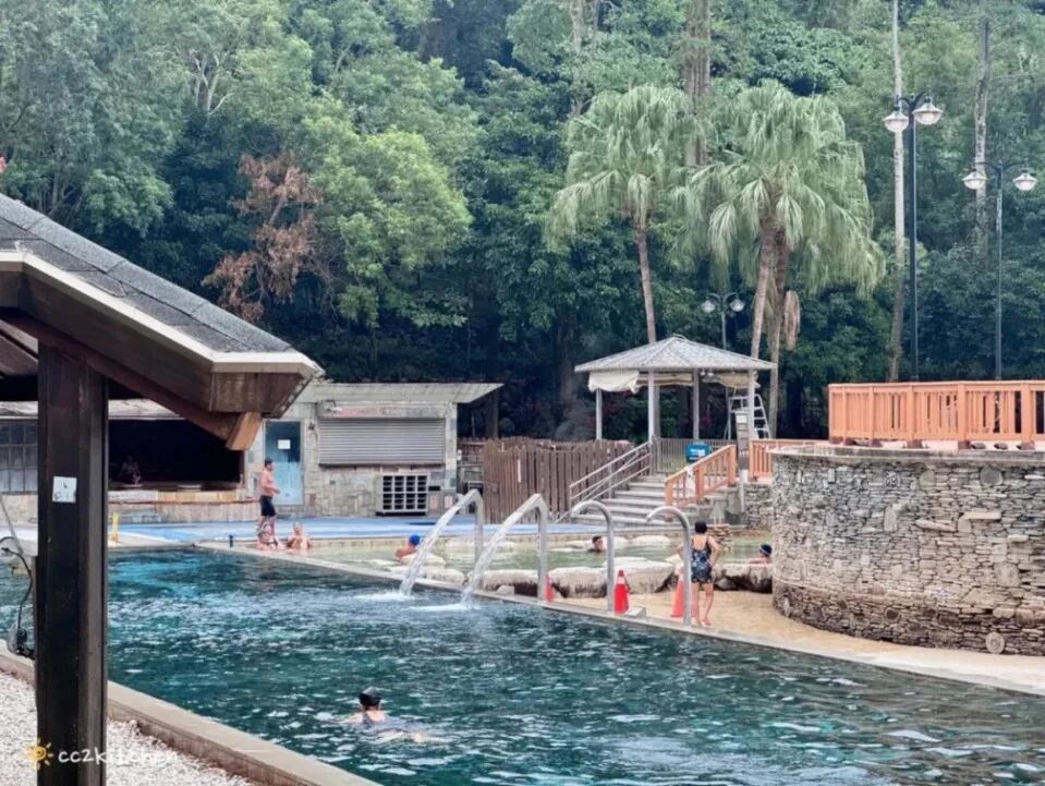 A serene outdoor hot spring pool at sunset, surrounded by lush tropical greenery.