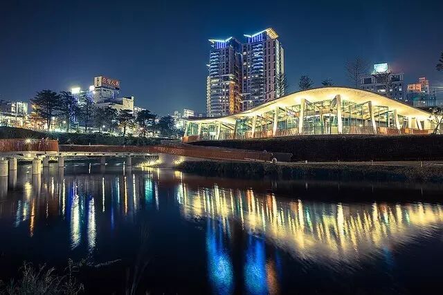 Night view of Qiuhonggu Plaza with beautifully illuminated paths and cityscape reflections on the water.