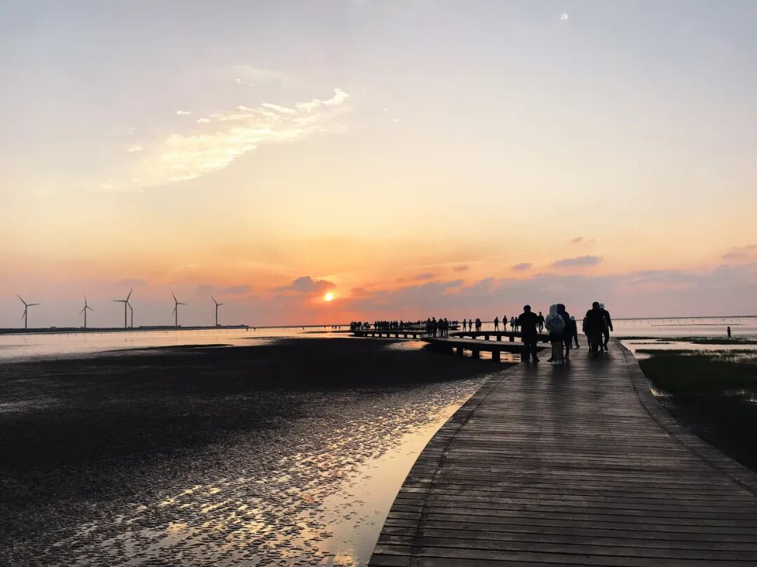 A solitary figure on the Gaomei Wetlands boardwalk, admiring fiery sunset reflections on tranquil tidal flats.