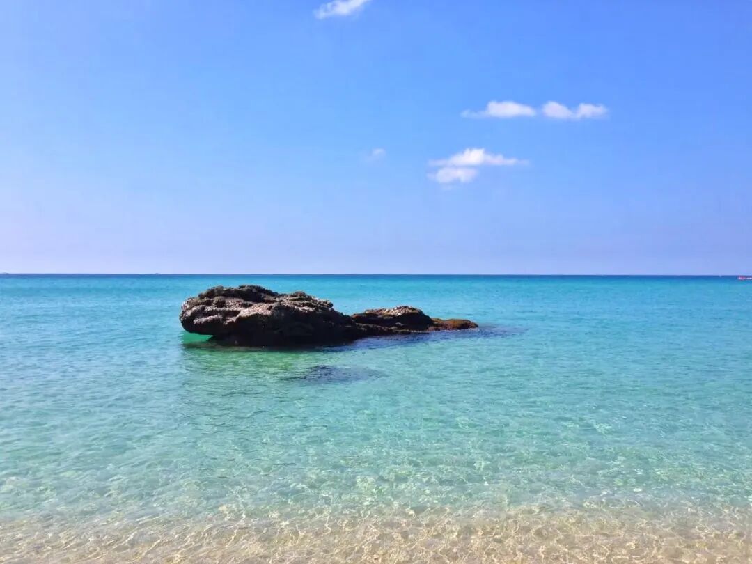 A person wading in the shallow, clear waters of Baishawan Beach on a sunny day