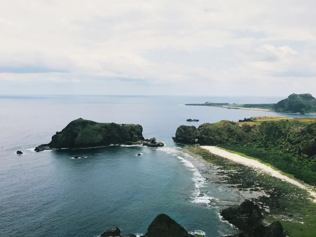Scenic view of Green Island's cliffs and waves under a cloudy sky.