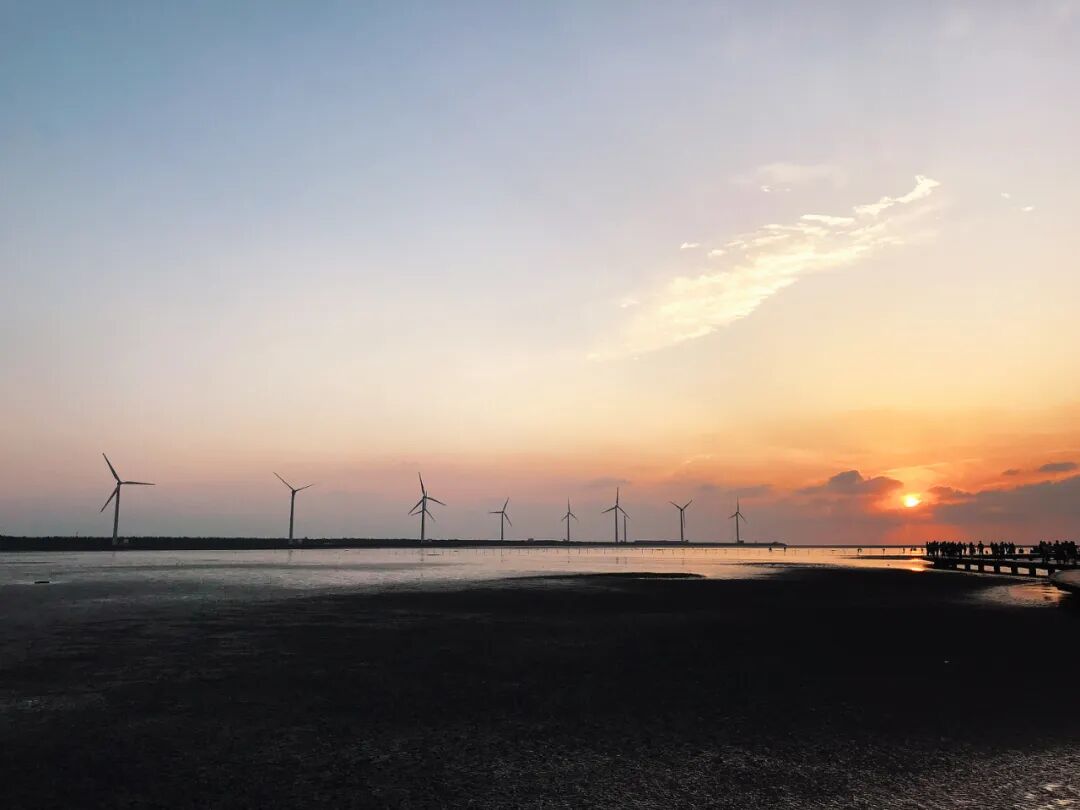 Majestic Gaomei Wetlands wind turbines silhouetted against a dramatic sunset, with the boardwalk stretching into the foreground.