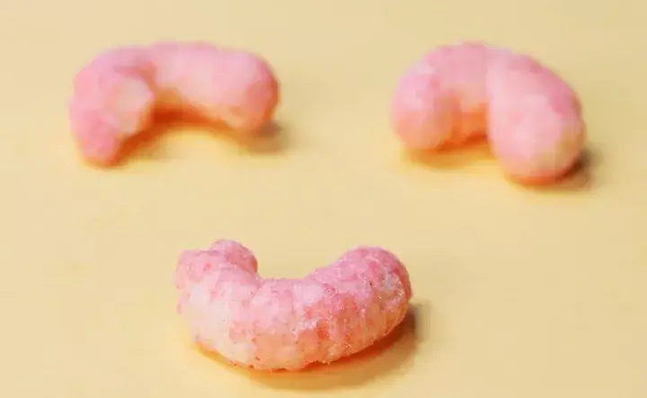 Another smiling curved Guai Guai snack piece, strawberry flavor